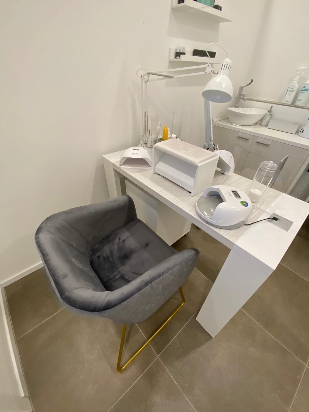 La postazione per mani e unghie: il tavolo bianco con le lampade e una poltroncina di velluto grigio con le gambe dorate